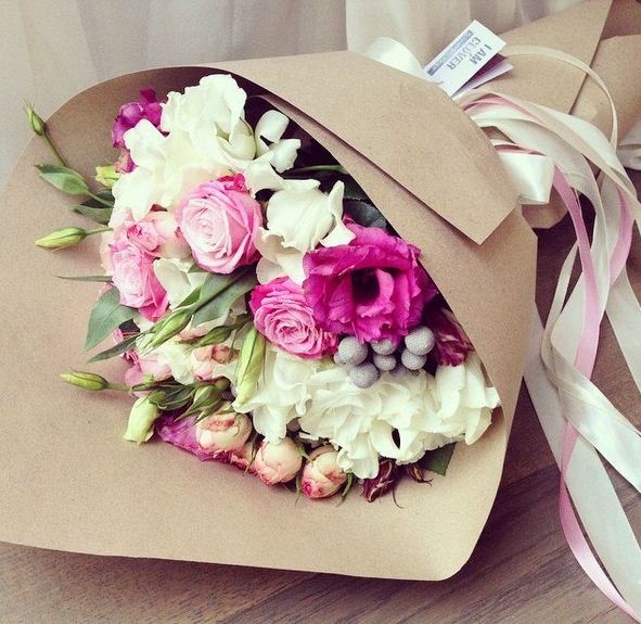 Букет цветов, упакованный в бумагу и украшенный лентами.